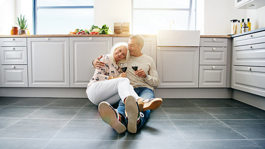 Paar sitzt in Küche auf warmem Fussboden und trinkt Wein