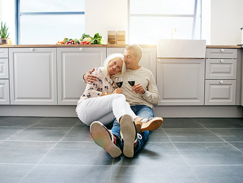 Paar sitzt in Küche auf warmem Fussboden und trinkt Wein
